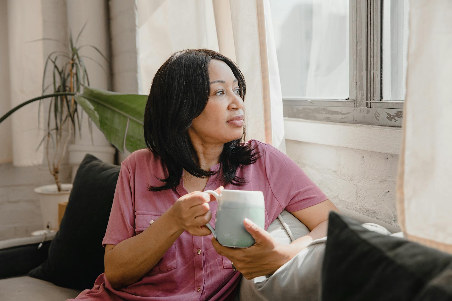 woman holding cup on sofa while in thought